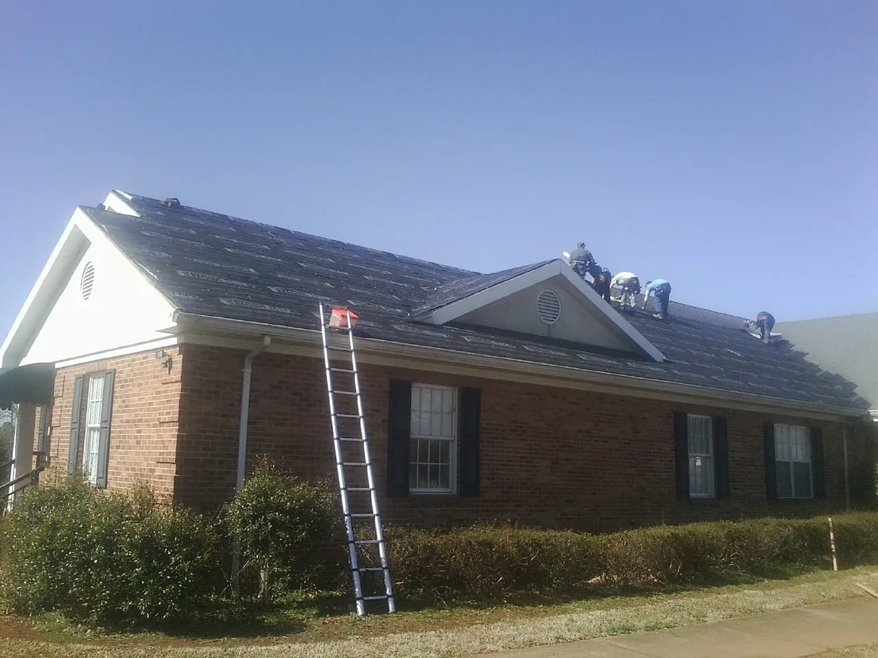 Crew tearing shingles off a brick ranch roof with a ladder set — Metal Roof Repair work by our crew in Cross Fork