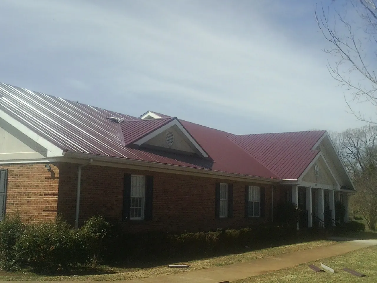 Red metal roof with gabled entries on a long brick building, from a Hail Damage Roof Repair job in Cross Fork