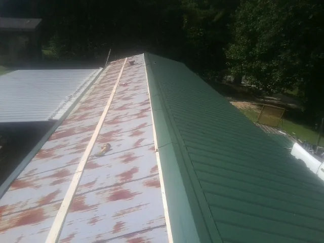 Old rusted panels beside newly installed green metal roofing — Wind Damage Roof Repair by Roofing Brothers in Cross Fork