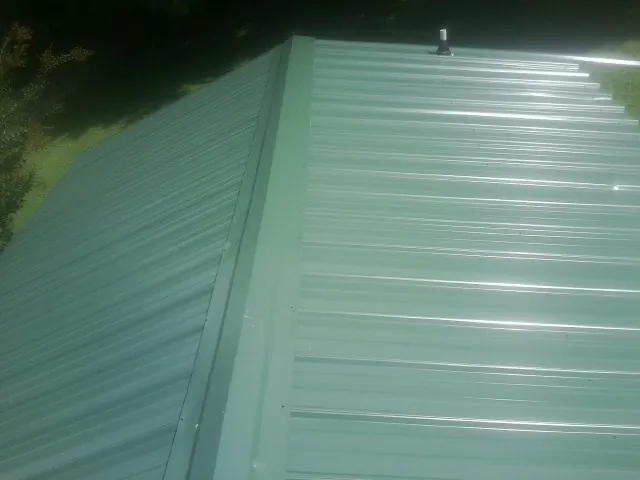 New green metal panels meeting at the ridge of a roof — Flat Roof Repair work by our crew in Cross Fork