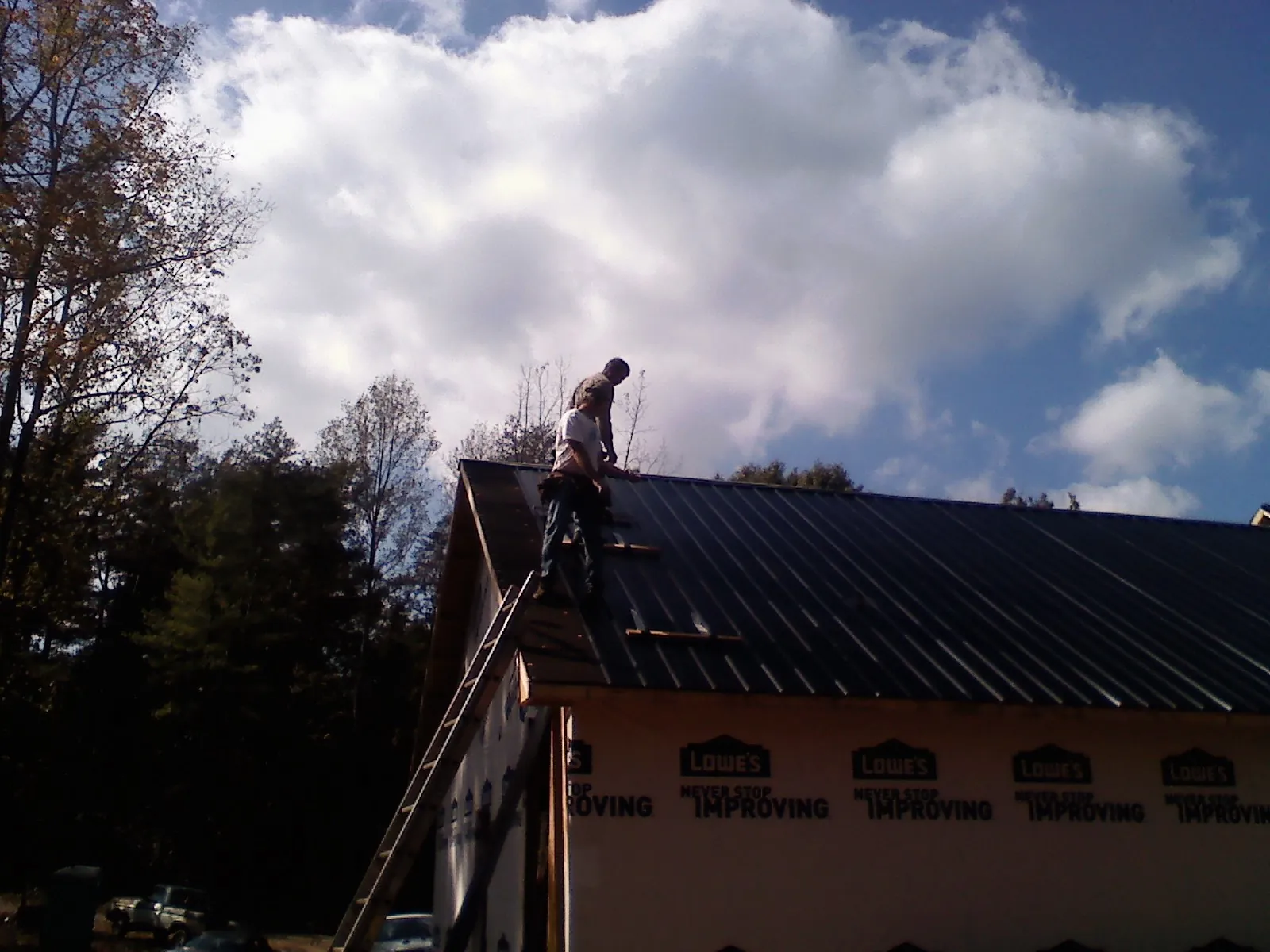 Roofer fastening dark metal panels high against a cloudy sky, from a Roof Inspection job in Cross Fork