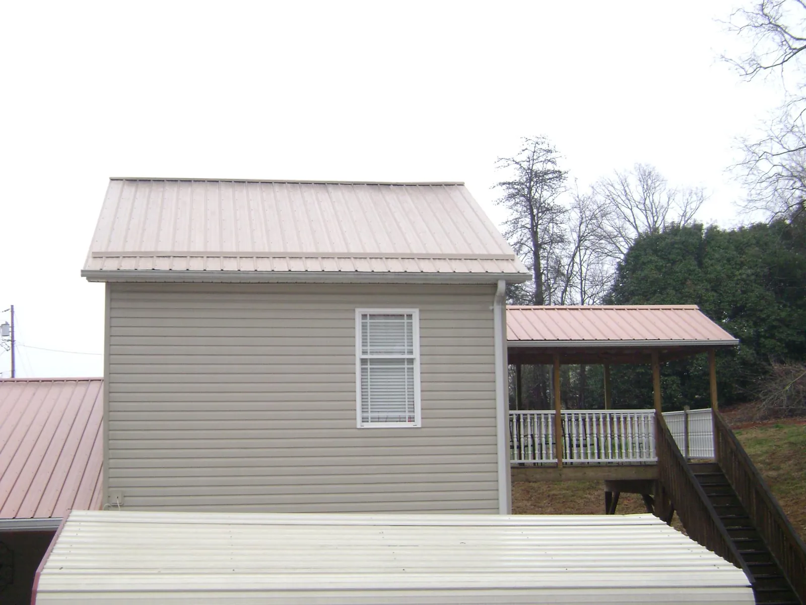 Tan metal roofs on a two story addition and attached porch, from a Roof Replacement job in Cross Fork